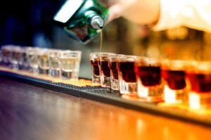 Bartender pouring strong alcoholic drink into small glasses on b